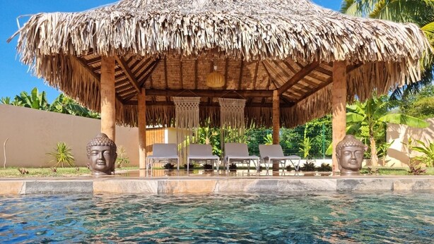 A pool area with a thatched-roof structure, lounge chairs, and Buddha statues. - In the heart of the village villa 6 people not 8 (Moorea)