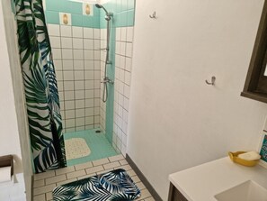 Ein Badezimmer mit Dusche, gefliesten Wänden, einer waschmaschinenmuster-Duschmatte und einem kleinen Waschbecken mit einer gelben Seifenschale.