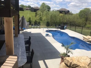 Um quintal com piscina, móveis de pátio e vista para casas ao fundo.