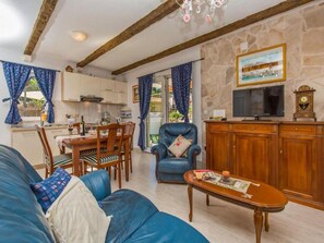 Una sala de estar acogedora con un sofá, una mesita de centro y un comedor con una mesa y sillas. Se observa una pared de piedra y un televisor sobre un mueble de madera.