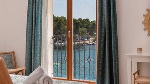 A hotel room with a large window, a bed with a patterned bedspread, a wooden chair, and a small table with a decorative item. - Mamma mia luxury rooms - Double Room with Sea View (Trogir)