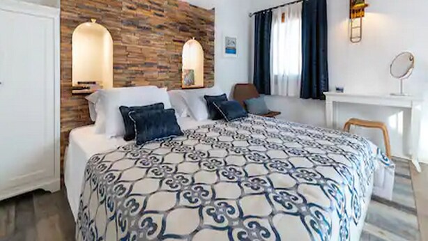 A bedroom with a patterned bedspread, a wooden accent wall, a desk with a mirror, and a window with curtains. - Mamma mia luxury rooms - Duplex Double Room with Sea View (Trogir)