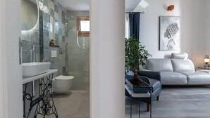 A modern bathroom with a glass shower enclosure, a white sink, and a toilet. There is a potted plant and a grey sofa in the living area. - Mamma mia luxury rooms - Duplex Double Room with Sea View (Trogir)