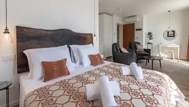 Une chambre d’hôtel avec un grand lit, une tête de lit en bois, une chaise, une petite table et une cheminée.