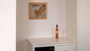 Un meuble blanc, avec une œuvre d’art encadrée au-dessus, et une bouteille dont l’étiquette se trouve sur le dessus.
