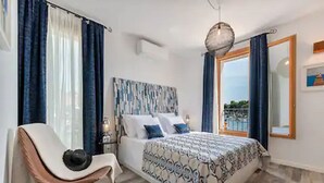 Ein Schlafzimmer mit einem Bett, einem Sessel, einem Nachttisch und einem großen Fenster mit Vorhängen.