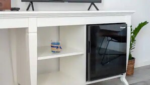 Ein weißes Schranksystem mit einem schwarzen Kühlschrank, einer Ablage mit einer Dose und einer Pflanze.