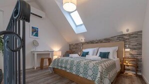 Een slaapkamer met een schuine kap, een bed met beddengoed met een patroon, een bureau en een stoel.
