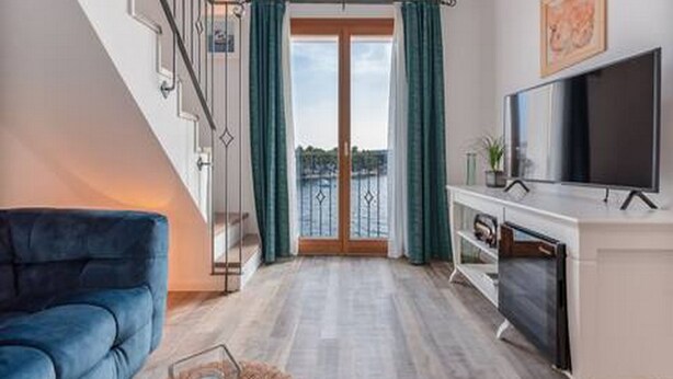 Een moderne woonkamer met een blauwe bank, een flatscreen televisie en een balkon met groene gordijnen.