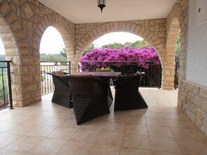 A covered patio area with a stone archway, a table with chairs, and purple flowers. - Apartment Villa Jakov - Two Bedroom Apartment with Terrace and Swimming Pool (Rogač)