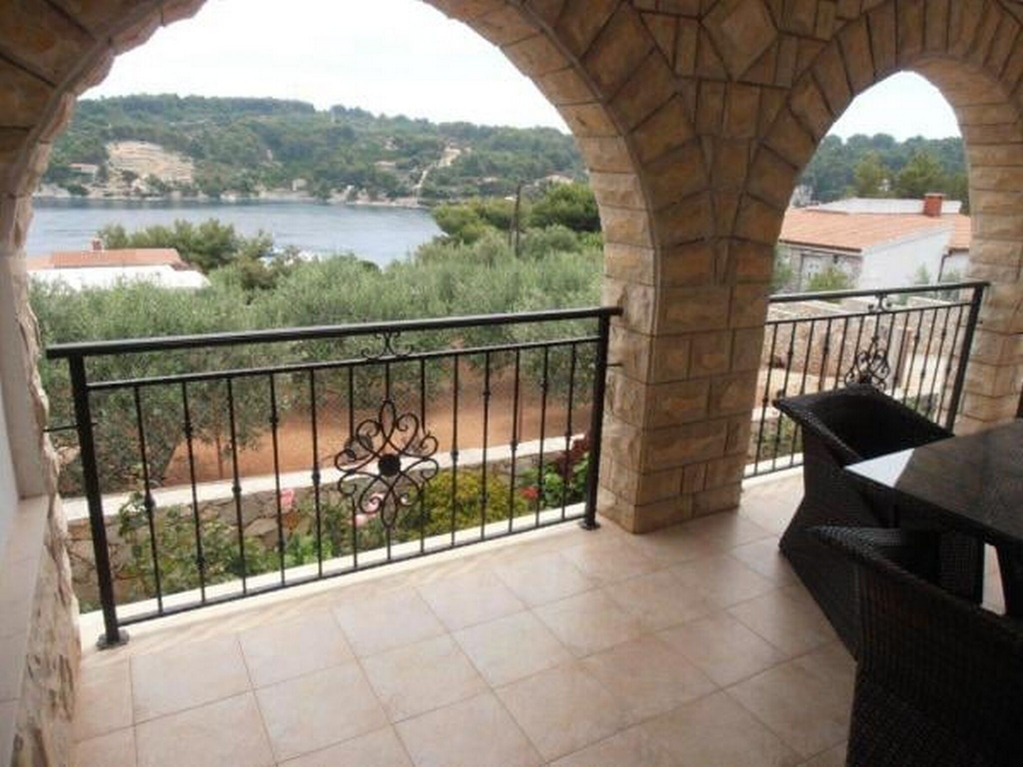 A balcony with stone arches, a metal railing, and a view of a lake and greenery.