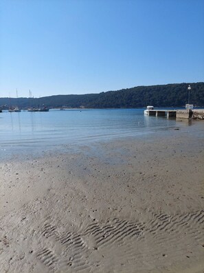 A sandy beach with boats docked in the background and a pier extending into the water. - Apartment Marta - One Bedroom apartment with pool (Rab)