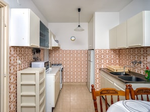 Une cuisine de taille réduite avec des meubles blancs, un dosseret à motifs et une chaise en bois.