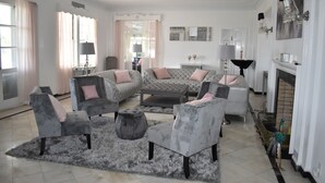 Un salón amplio con una paleta de colores gris y blanco, que incluye un sofá grande, sillones, una mesa de centro y una chimenea.