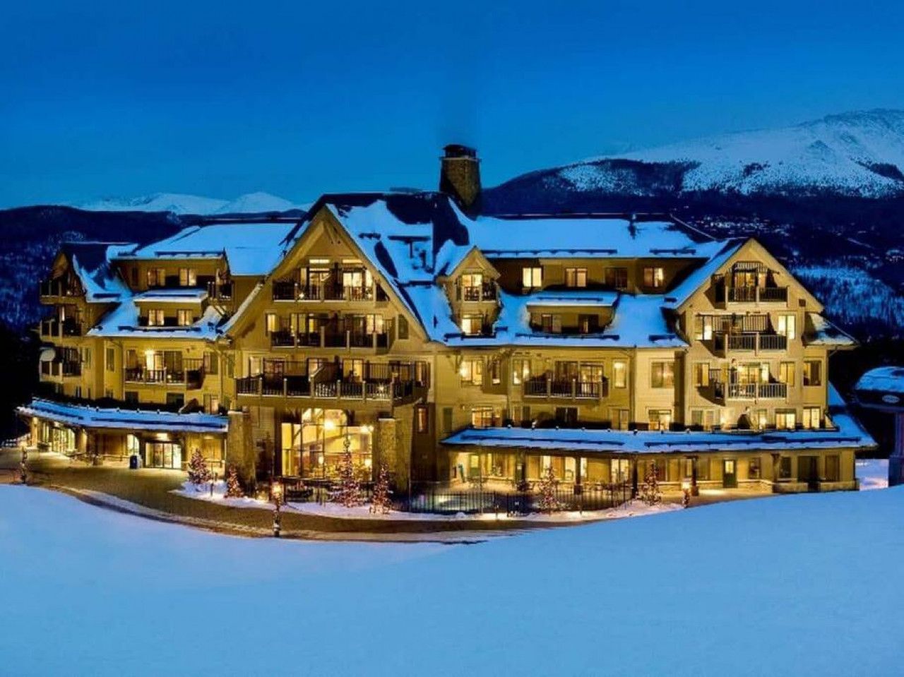 Un grand hôtel à plusieurs étages, doté d’une façade symétrique, de nombreux balcons et, en arrière-plan, d’un paysage enneigé.