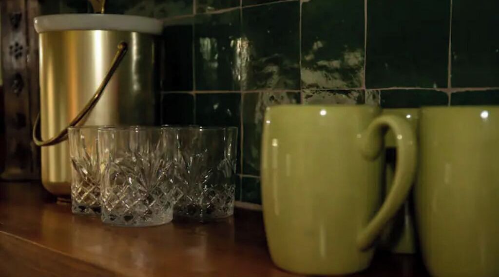 A kitchen counter with a stainless steel pot, a glass container, and two green mugs.