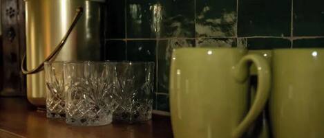 A kitchen counter with a stainless steel pot, a glass container, and two green mugs.