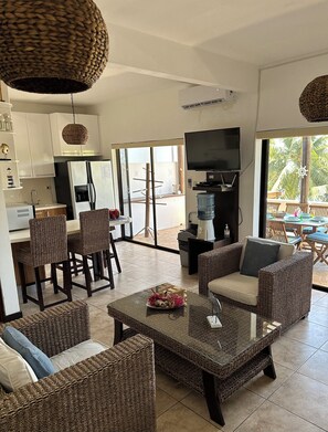 A modern living space with wicker furniture, a flat-screen TV, and a kitchen area.