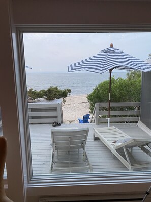 Une terrasse dotée de deux chaises longues et d’un parasol à rayures, offrant une vue sur la plage.