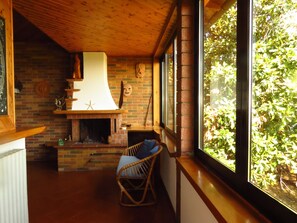 A cozy room with a brick fireplace, a wicker chair, and a large window overlooking greenery.