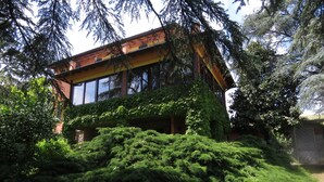Ein modernes Gebäude mit großen Fenstern und einem Balkon, umgeben von üppiger Vegetation.
