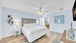 Une chambre à coucher comprenant un lit, un ventilateur de plafond, une lampe fixée au mur et un élément décoratif mural.