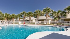 Une piscine entourée de palmiers et délimitée par une clôture blanche.