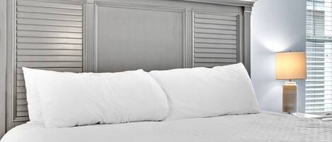A neatly made bed with white linens and pillows, a wooden headboard, and a bedside lamp.