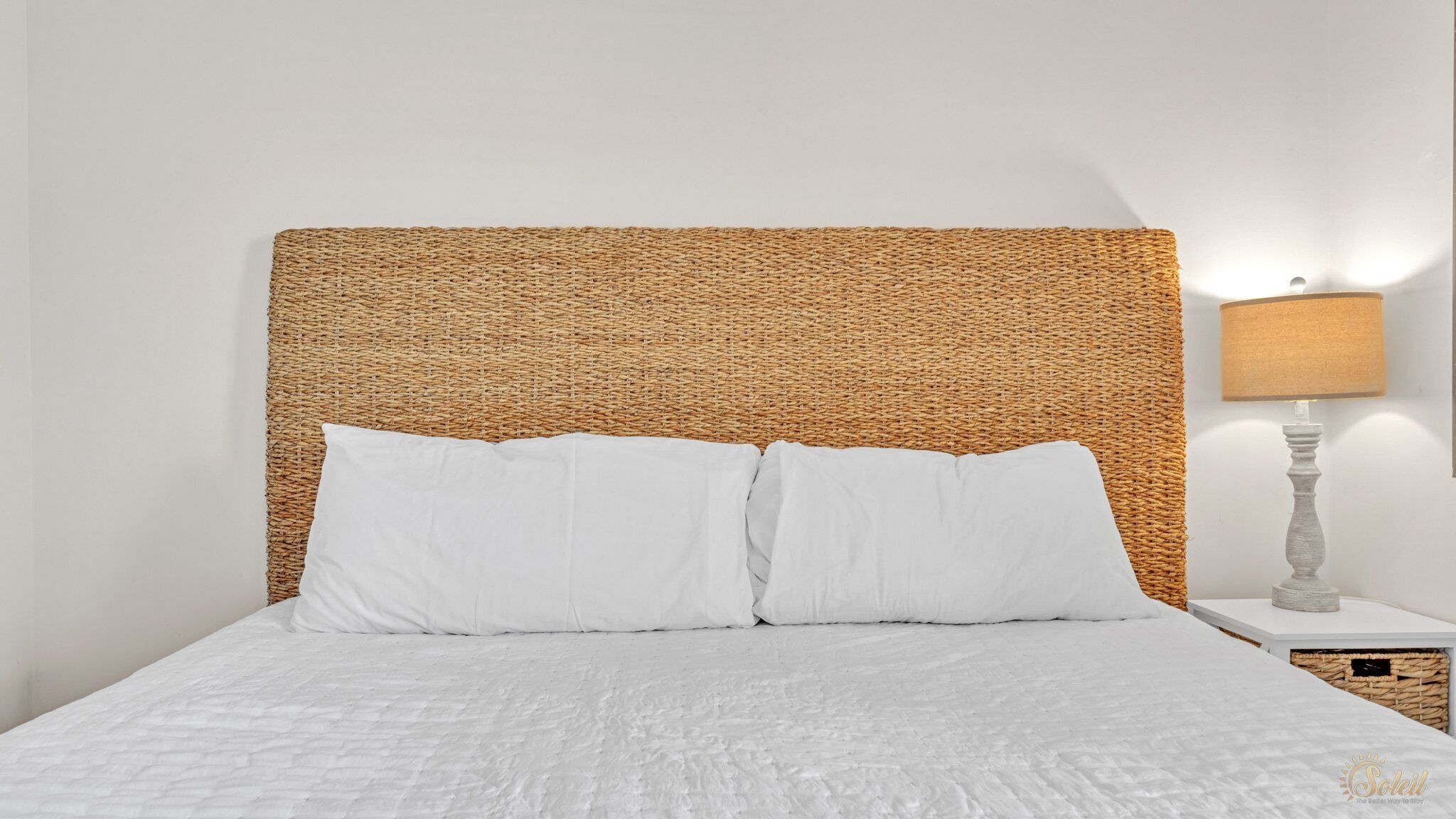 A bed with a woven headboard, white pillows, and a white quilted bedspread.