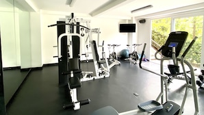 Une salle de sport équipée de matériel d’exercice, d’un tapis de course et d’un mur recouvert de miroirs.