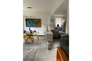 A modern kitchen with a dining area, featuring a large abstract painting, a trash bin, and a TV.