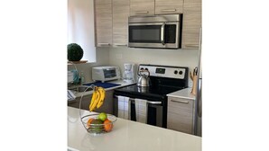Une cuisine moderne équipée d’appareils électroménagers en acier inoxydable, d’un four à micro-ondes, d’une bouilloire et d’un panier à fruits posé sur le plan de travail.