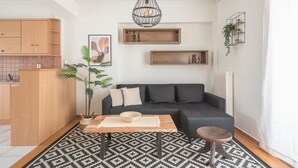 Un salon moderne avec un canapé noir, une table basse en bois, un tapis à motifs et un luminaire suspendu.