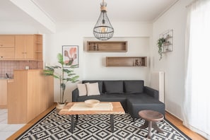 A modern living room with a black sofa, wooden coffee table, patterned rug, and a hanging light fixture.