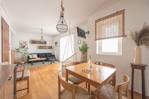 A modern living space with a dining area, a sofa, and a TV mounted on the wall.