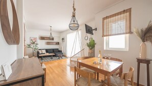 Un salon moderne avec une table à manger en bois, des chaises, un canapé et un luminaire suspendu.