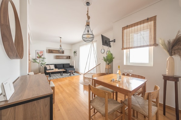A modern living room with a wooden dining table, chairs, a sofa, and a hanging light fixture.