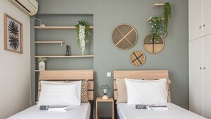 Une chambre avec deux lits, des têtes de lit en bois, une table de chevet avec une lampe, et des étagères murales ornées de plantes et d’objets décoratifs.
