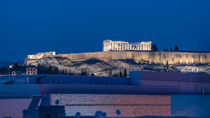 A historical building with classical architecture, situated on a hill with modern buildings in the foreground.