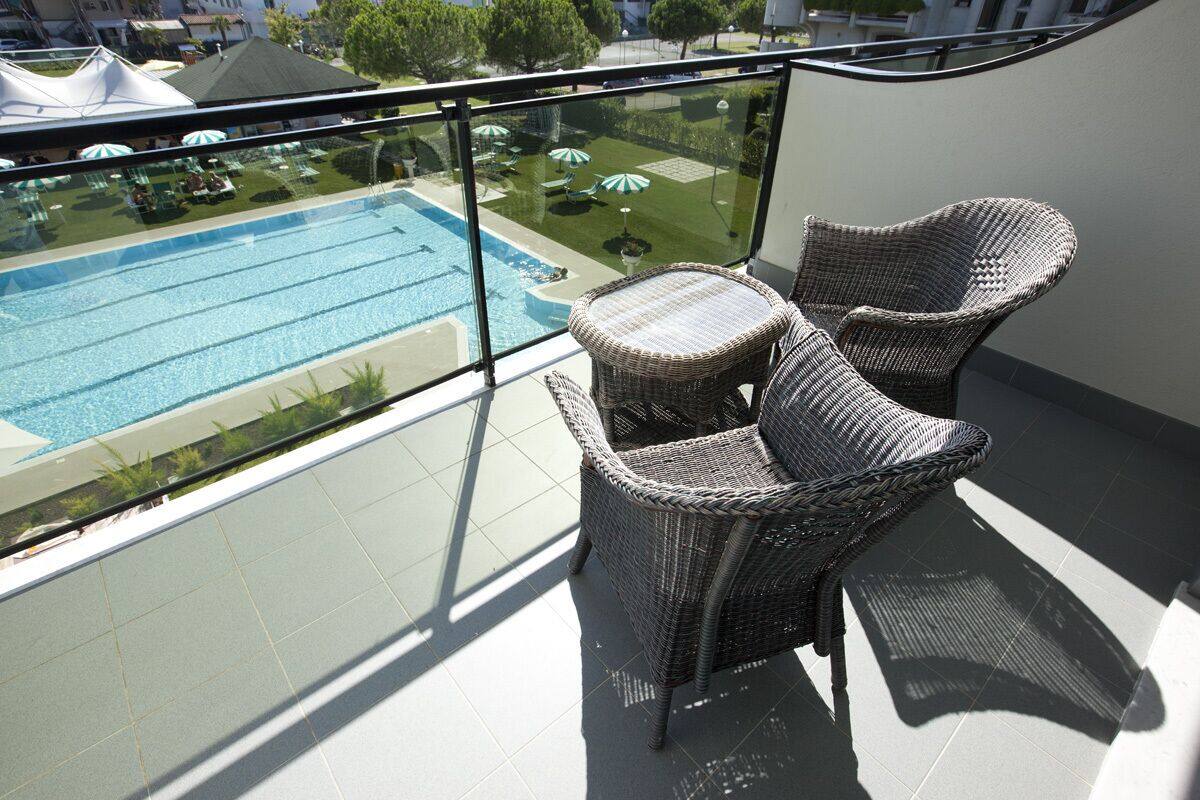 Un balcon doté de chaises en osier et d’une rambarde en verre, donnant sur une piscine agrémentée de parasols.