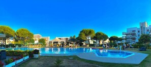 A swimming pool area with multiple pools, surrounded by greenery and buildings. - Hotel Falcone (Lignano Sabbiadoro)