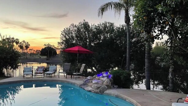 Una piscina con lettini prendisole e un ombrellone rosso, circondata da alberi e con vista sul tramonto.