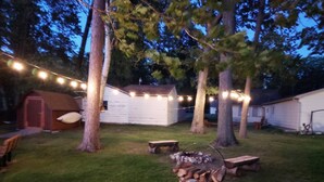 A backyard with a fire pit, picnic table, and string lights.