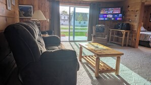A cozy cabin-style room with a sofa, a wooden coffee table, a TV mounted on the wall, and a sliding glass door leading to a patio.