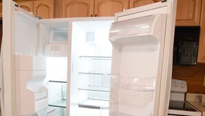 An open refrigerator with multiple shelves and a microwave above it.
