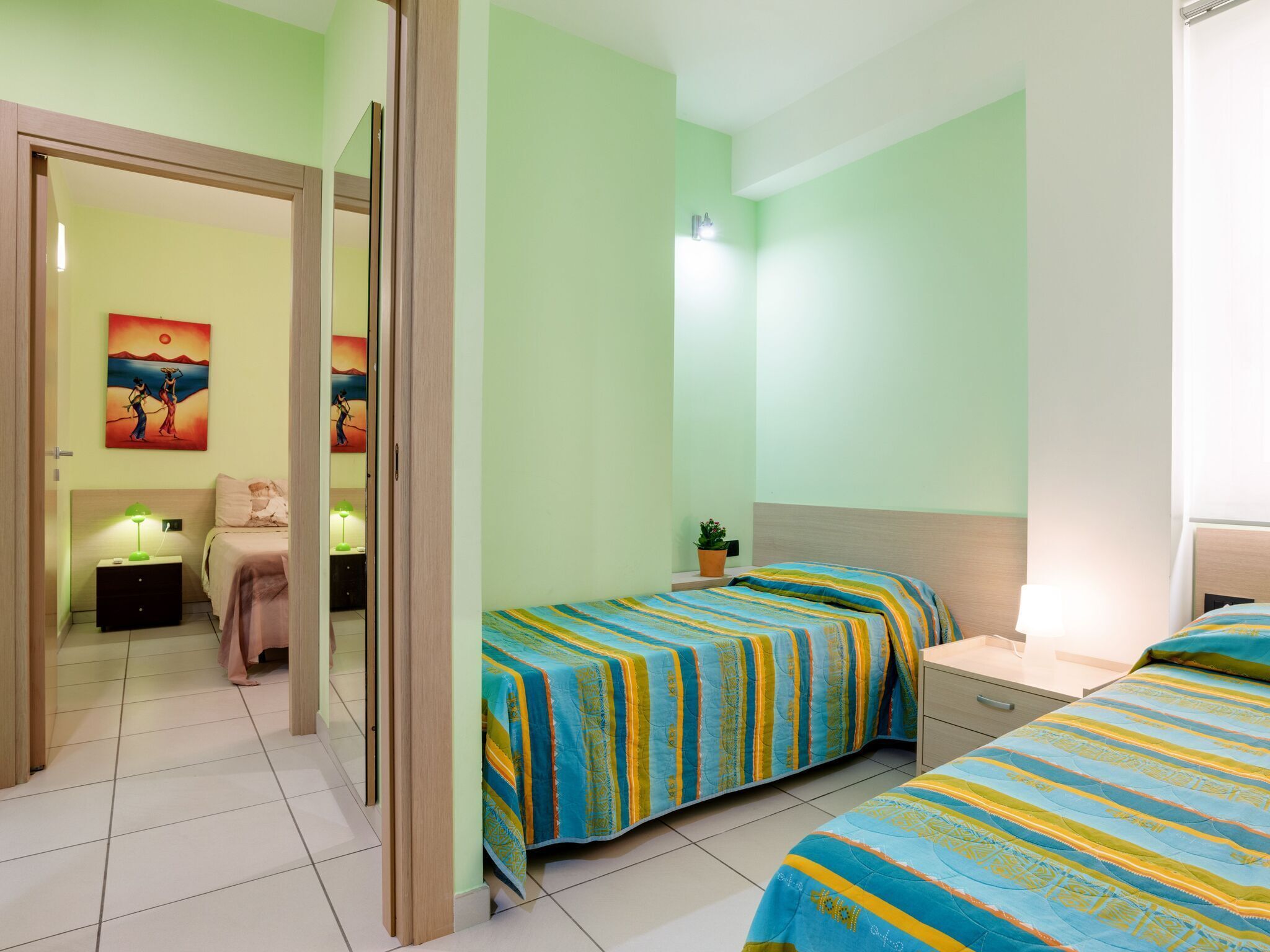A room with two beds, a nightstand, a small table, and a potted plant.