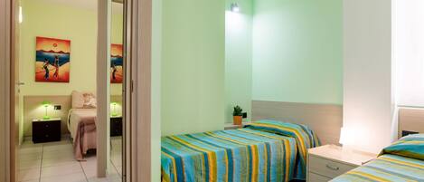 A room with two beds, a nightstand, a small table, and a potted plant.