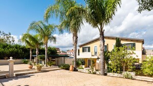 A two-story house with a paved courtyard, surrounded by palm trees and potted plants. - For a dream vacation to the Ionian Sea 5 sails (San Lorenzo  Reitani)