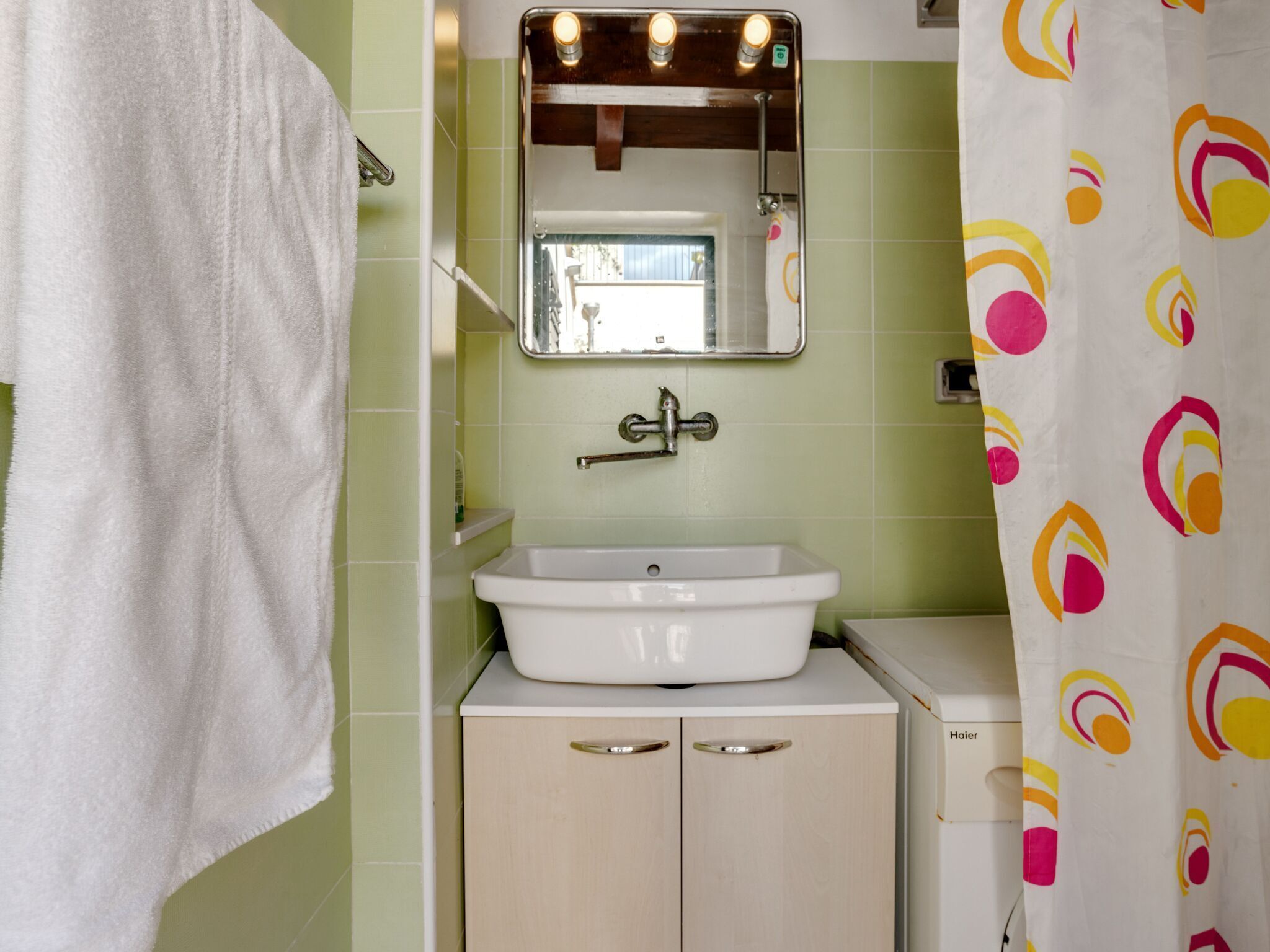 Un baño con un lavamanos blanco, un espejo encima y una cortina de ducha con un estampado colorido.