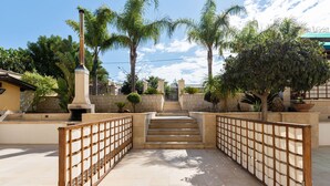 A paved pathway leading to a set of stairs, flanked by wooden fences and surrounded by palm trees and greenery. - For a dream vacation to the Ionian Sea 5 sails (San Lorenzo  Reitani)